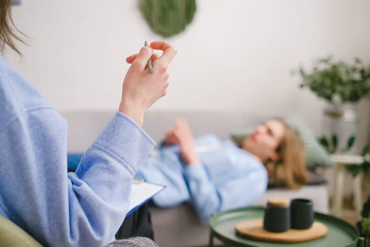 A practitioner holding their hands above a client resting in a bright, plant-filled room