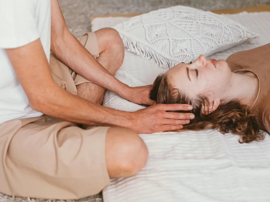 A practitioner holds their hands above a woman resting on a treatment bed