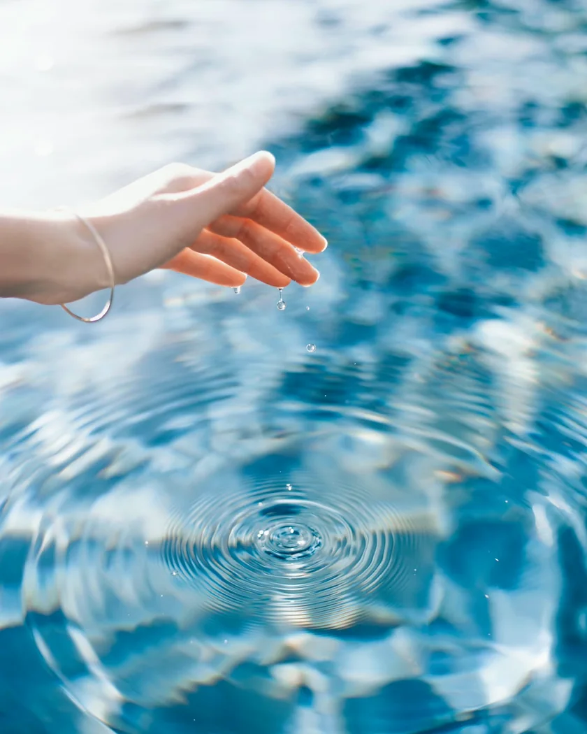A hand held just above still water, sending out gentle ripples